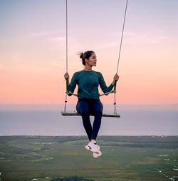 Full length of woman on swing at sunset