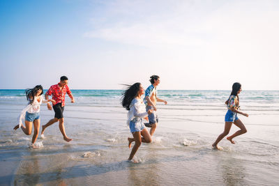 Friends running at beach against sky