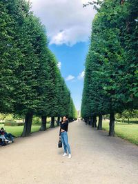 Woman standing on footpath amidst trees against sky