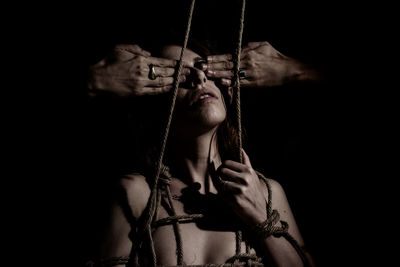 Cropped hand closing eyes of woman tied by rope against black background