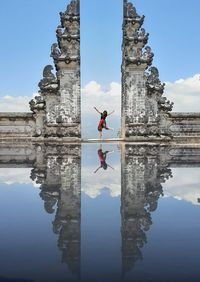 Woman reflecting on water while dancing by old wall