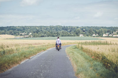 Rear view of man riding motorcycle on road against sky