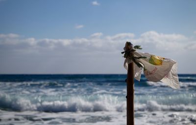 Flag of plastic and wooden pole by sea against cloudy sky