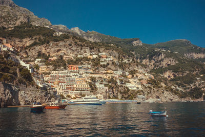 Sailboats in sea by buildings against clear blue sky