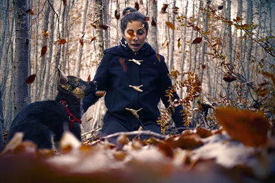 Woman and dog with leaves in mid-air at forest during autumn