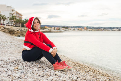 Portrait of smiling young woman sitting on beach against sky