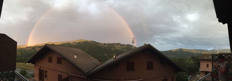 Rainbow over houses against cloudy sky