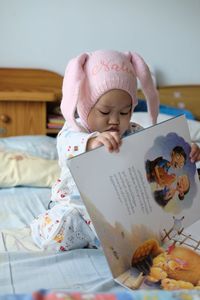 Cute baby girl sitting on bed at home