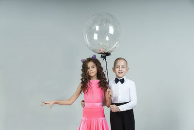 A curly-haired girl and a boy engaged in ballroom dancing pose with balloons in a photo studio