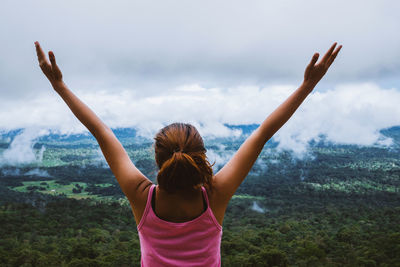 Rear view of woman with arms raised standing against forest