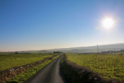 Road amidst field against clear sky