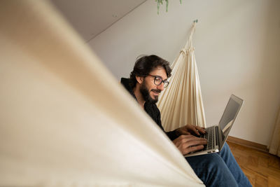 Young man  black glasses working with laptop on a white hammock notebook for working. home office