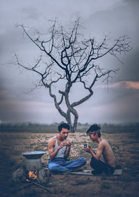 Friends having coffee against bare tree while camping during sunset