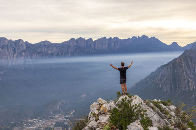 Rear view of man standing on mountain against sky