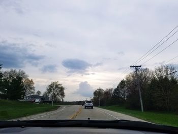 Cars on street against sky seen through windshield