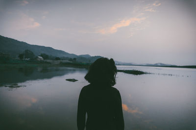 Rear view of silhouette woman standing by lake