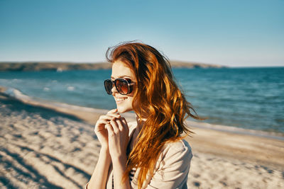 Young woman wearing sunglasses on beach against sky