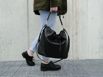 Low section of woman holding purse while walking on metal grate