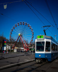 Cable car on street by ferris wheel against blue sky