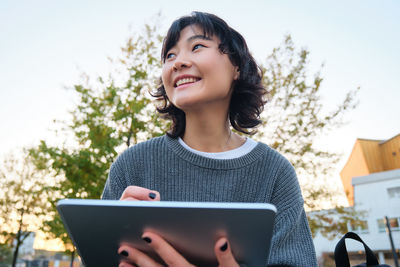 Portrait of young woman using laptop while standing against trees