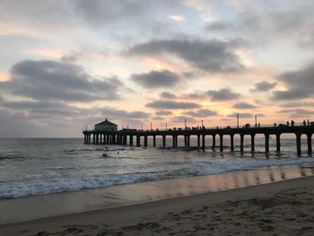 Pier on beach against sky during sunset