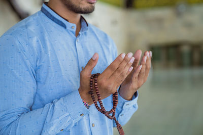 Midsection of young man wearing skull cap praying at mosque