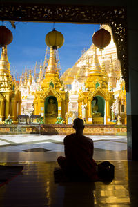 Rear view of man sitting outside temple against building