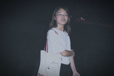 Portrait of young woman standing against black background