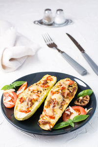 Ready-to-eat baked zucchini halves filled with cheese and tomato and basil leaves and cutlery