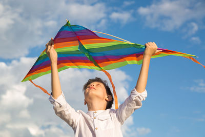 A teenage boy with a smile launches a bright kite into the sky on a summer day.