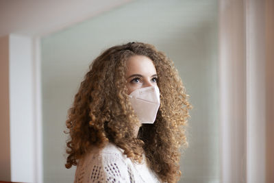 Portrait of young woman with curly hairs and sad eyes in white medical protective face mask 