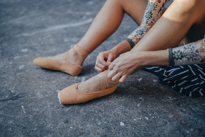 From above side view of crop ballerina sitting on gray floor and putting on pointe while preparing for training in studio