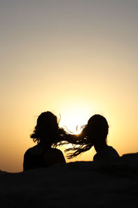 Silhouettes of two heads of young woman back with hair in the wind at sunset, copy space