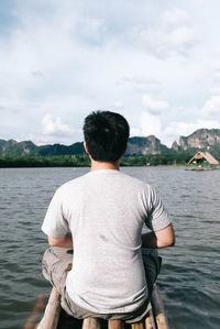 Rear view of man sitting on wooden raft over lake against sky