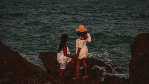 Rear view of woman sitting on rock by sea