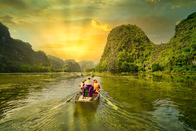 People in boat on river against sky during sunset