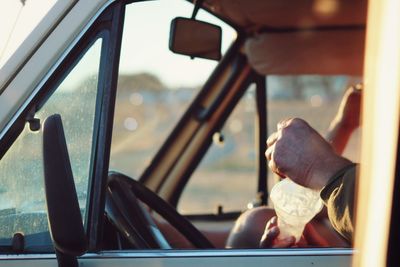 Cropped hands of man holding container in car seen through window