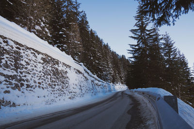 Snow covered road by trees against sky