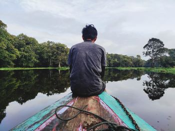 Rear view of man looking at lake against sky