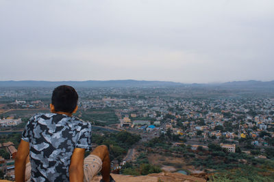 Rear view of man looking at city buildings against sky