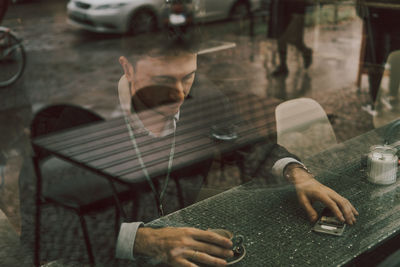 Young man holding drink seen through window