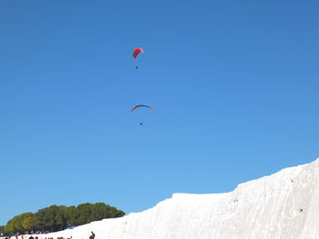 Low angle view of people paragliding against clear blue sky