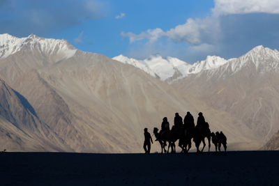 Silhouette people riding camels in desert against mountains