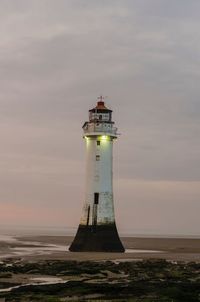 Lighthouse by sea against sky during sunset