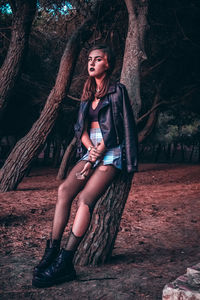 Young woman looking away while sitting on tree trunk