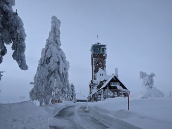 Traditional windmill on snow covered building against sky