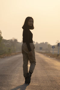 Side view of young woman standing on road against sky