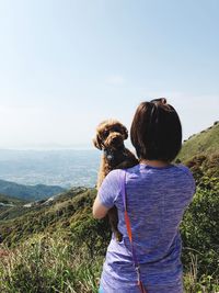 Rear view of woman with dog standing on mountain against sky