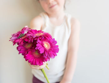 Close-up of woman holding pink flower against white background