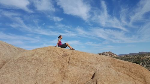 Low angle view of woman sitting on rock against sky